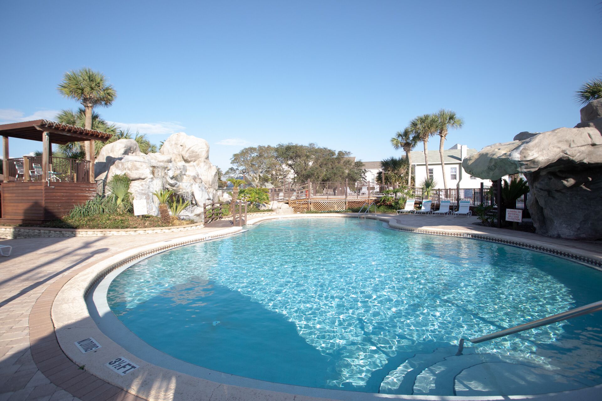 Une piscine d’un bleu éclatant, avec une terrasse en bois et des palmiers.