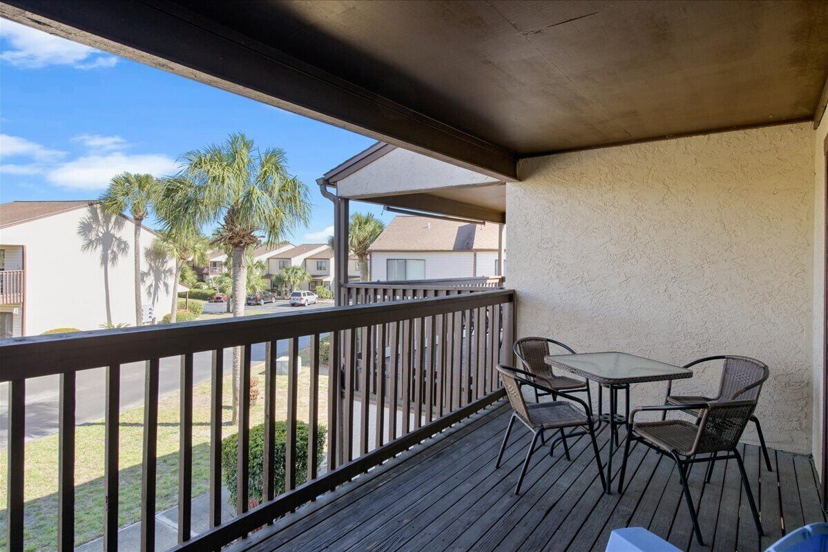 Un balcón con mesa y sillas, con vistas a una zona residencial con palmeras y casas.