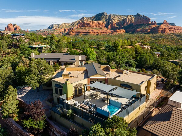 A modern house with a swimming pool, surrounded by lush greenery and red rock formations in the background.