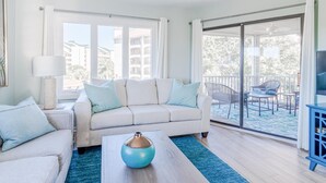 Una sala de estar moderna con un sofá blanco, una mesa de centro y vistas a un balcón con mobiliario exterior.