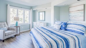 Un dormitorio con una cama grande, una silla, un tocador y una ventana con cortinas.