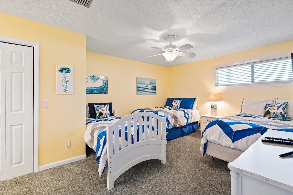 A bedroom with two beds, a ceiling fan, and artwork on the walls.