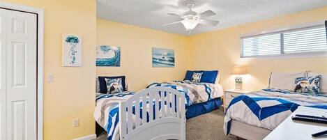A bedroom with two beds, a ceiling fan, and artwork on the walls.