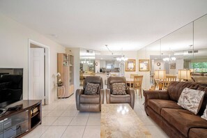 Un salón amplio con un sofá de cuero marrón, dos sillones de cuero, un televisor y un comedor con muebles de madera.