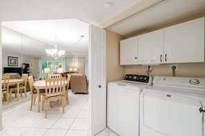 Una cocina funcional con lavadora, un comedor con mesa y sillas, y vistas al exterior a través de una ventana.