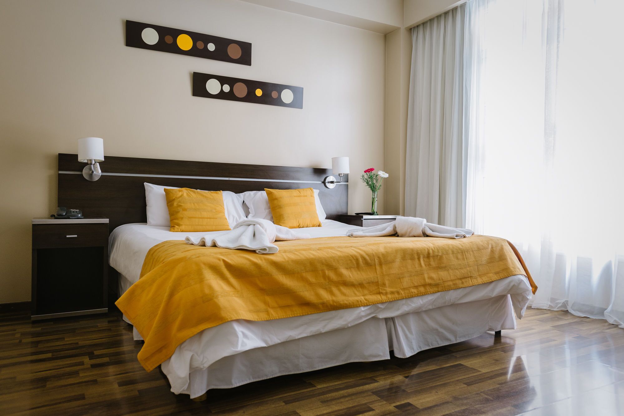 A neatly made bed with a yellow and white bedspread, a wooden headboard, and two wall-mounted light fixtures.