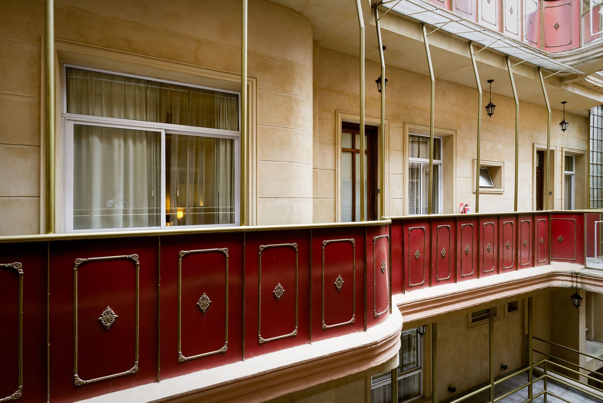 A multi-story building with a red balcony railing, large windows with curtains, and a classic architectural style.