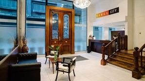 A hotel lobby with a wooden reception desk, a staircase, and a seating area with a chandelier.