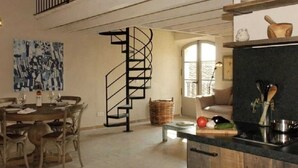A dining area with a spiral staircase, a dining table set with chairs, and a kitchen counter with vegetables. - Splendid duplex in Provence, in the middle of vineyards (Robion)