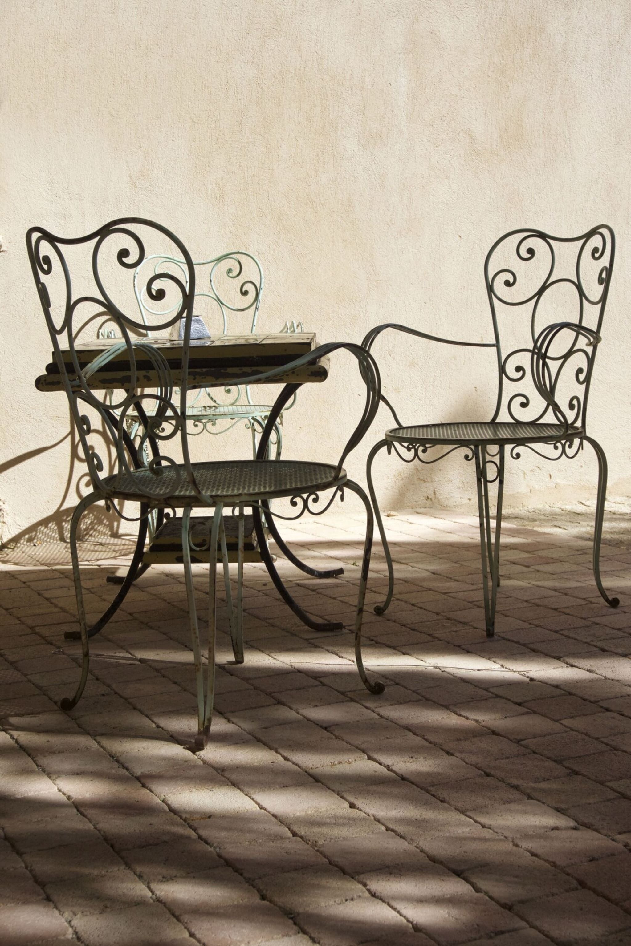 Une table en métal et deux chaises aux motifs complexes, posées sur un sol carrelé, devant un mur uni.