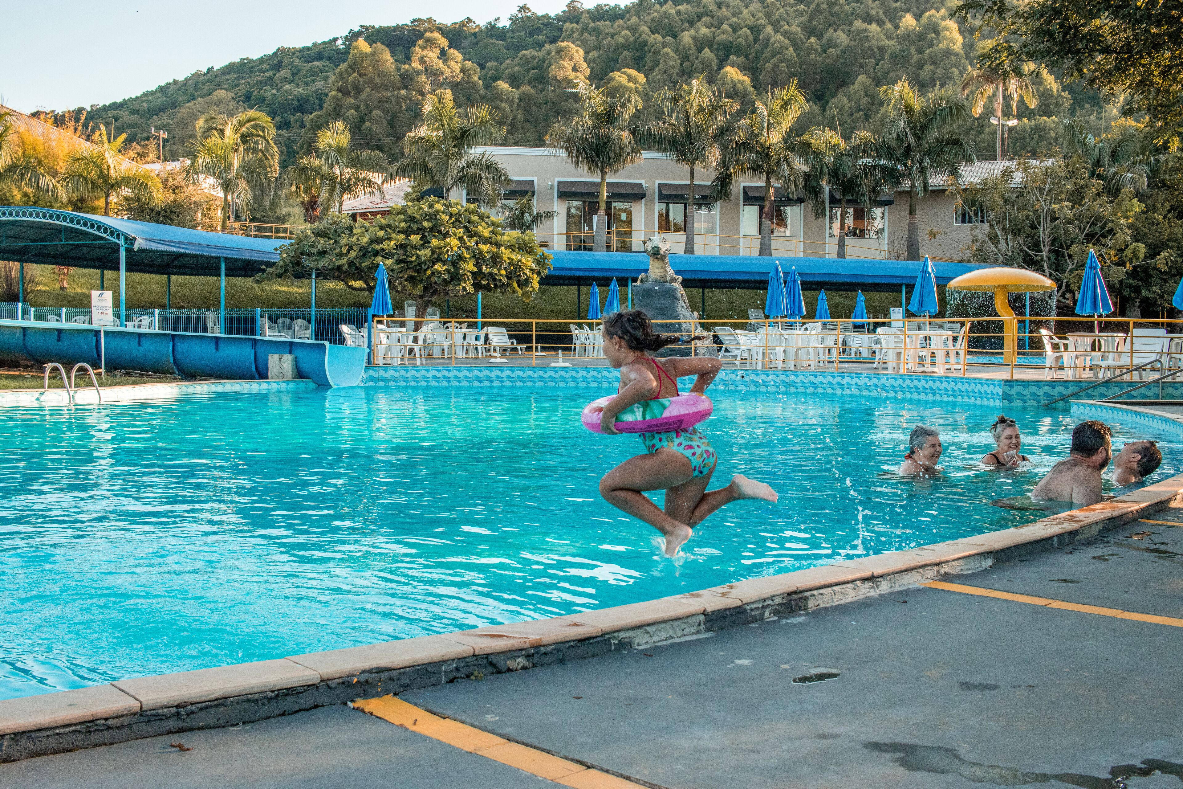 Piscina com trampolim, espreguiçadeiras e guarda-sóis.