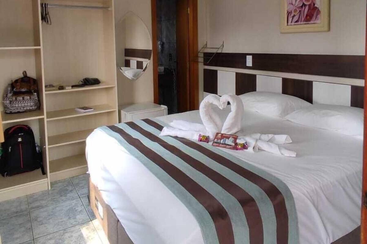 A hotel room with a bed, a wardrobe, a television, a painting, and a ceiling light.