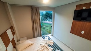 Ein Hotelzimmer mit Bett, Fenster mit Blick auf einen Balkon und einem an der Wand befestigten Fernseher.