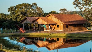 Ein rustikales Holzhaus mit rotem Dach, einer Veranda und einem Teich davor.