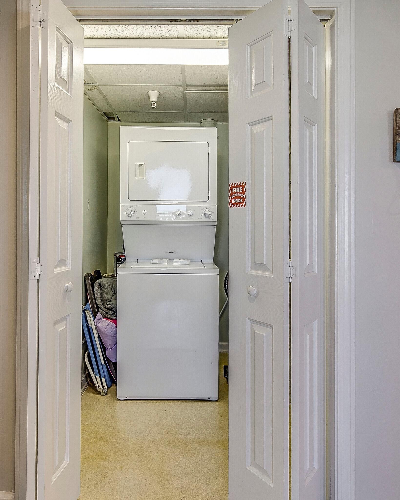 A laundry room with a white washer and dryer, a fire extinguisher sign, and a door leading to another room.