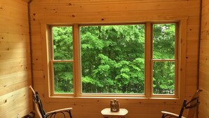 Una habitación de cabaña de madera con un ventanal grande, dos mecedoras y una mesita.
