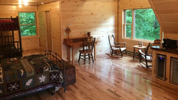 Interior acogedor de una cabaña con literas, un escritorio, sillas mecedoras y ventanas amplias que ofrecen vistas al bosque.