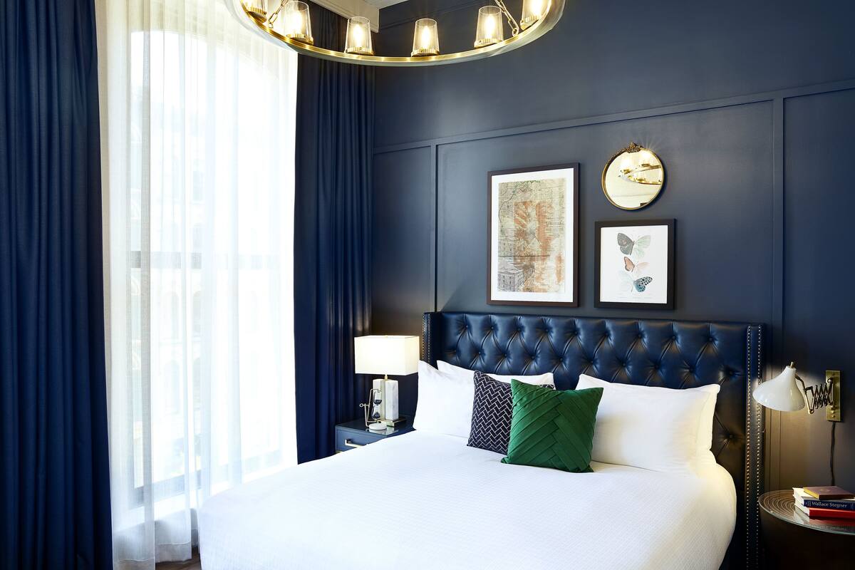A neatly made bed with a tufted headboard, a bedside lamp, and a framed map and butterfly picture on the wall.