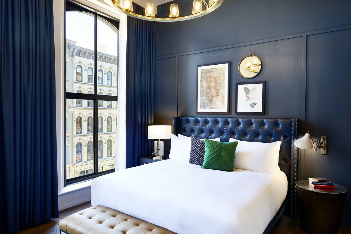 A neatly made bed with a tufted headboard, a bedside lamp, and a nightstand with a book and a framed picture.