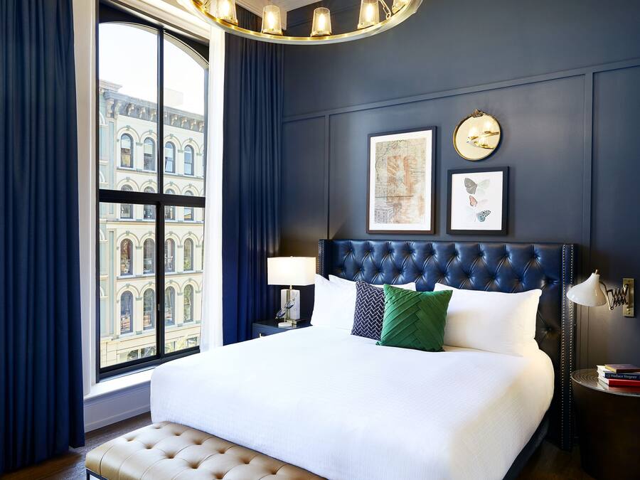 A neatly made bed with a tufted headboard, a bedside lamp, and a nightstand with a book and a framed picture.