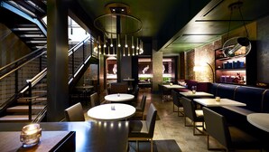 A modern restaurant interior with a staircase, round tables, and a brick wall. - The Grady (Louisville)