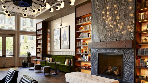 A modern interior with a fireplace, bookshelves, a green sofa, and leather chairs. - The Grady (Louisville)