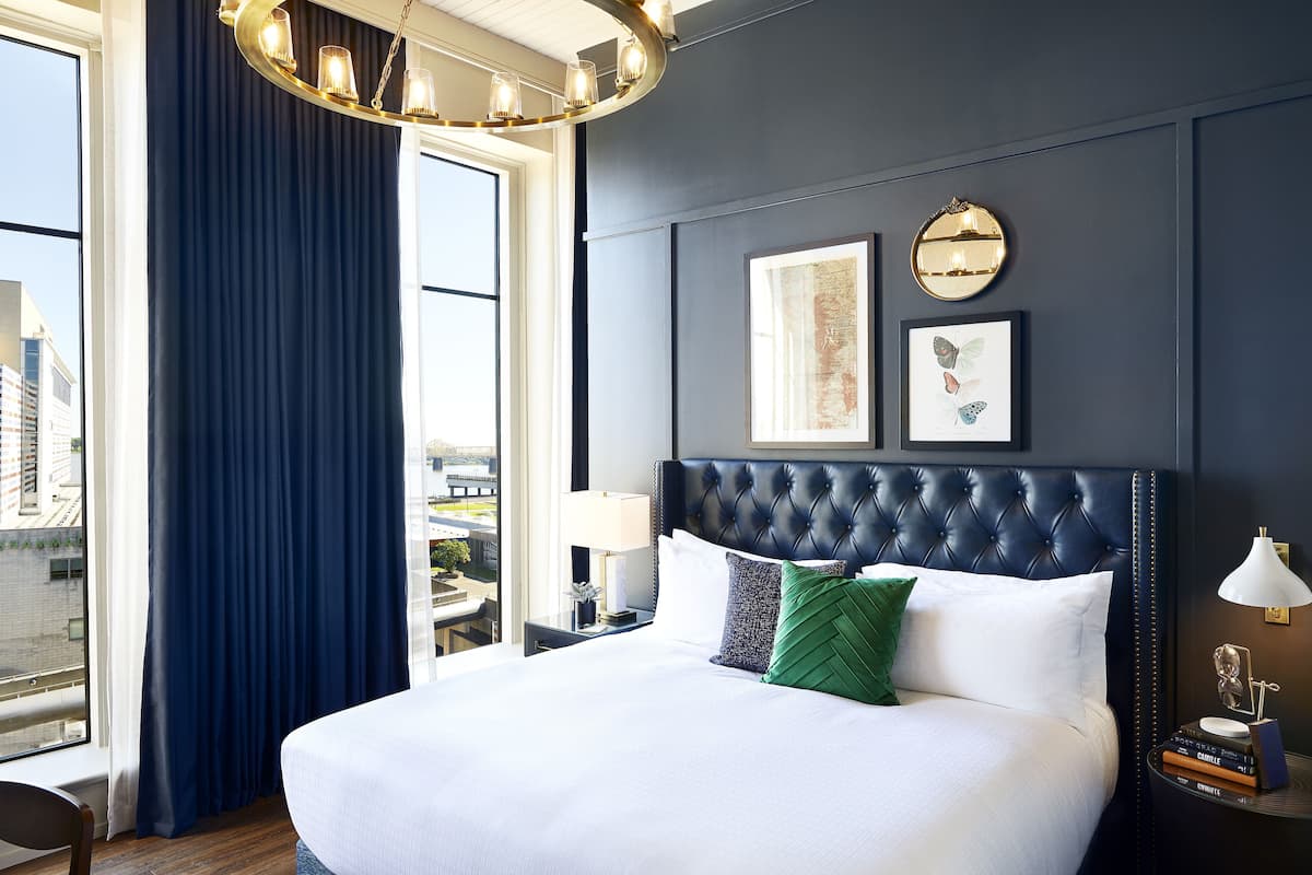 A hotel room with a large bed, a view of the city, a chandelier, and framed artwork on the wall.