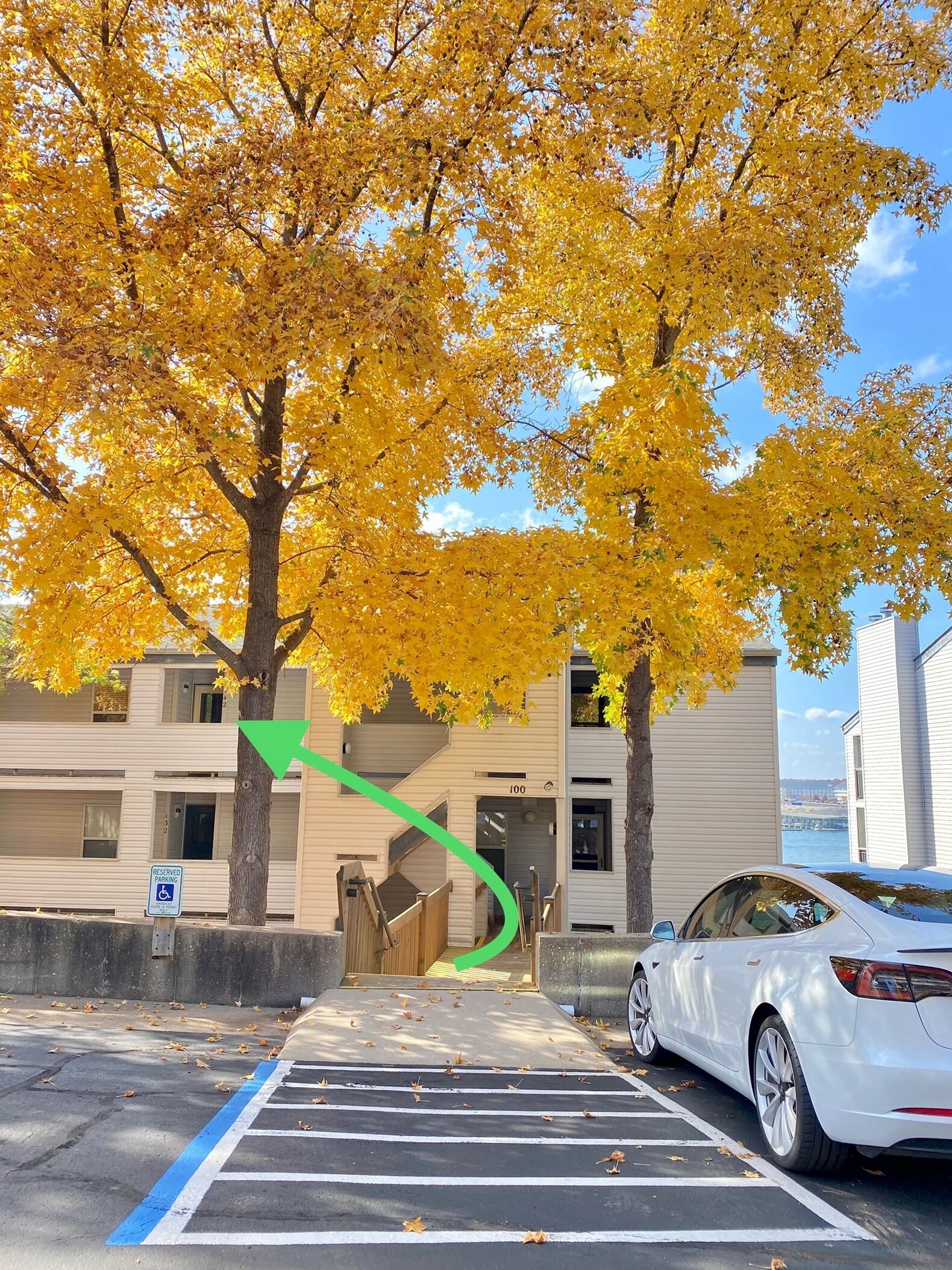 Une zone de stationnement avec un panneau indiquant qu’elle est réservée, l’entrée d’un bâtiment et une voiture blanche garée à proximité.