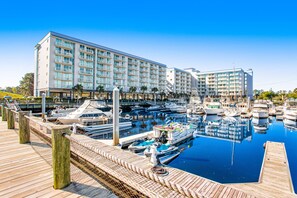 A marina with multiple boats docked, a large hotel building, and a wooden walkway. - 3rd floor condo with hot tub, central AC, private W/D, & marina view (North Myrtle Beach)
