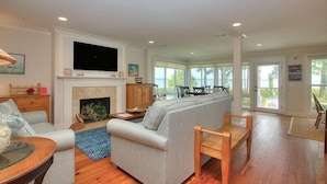 A spacious living room with a fireplace, a large sofa, and a television mounted on the wall.