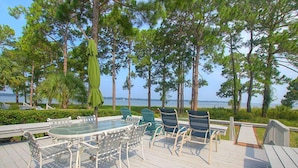 A deck with a glass-top table and chairs, overlooking a body of water and surrounded by trees.