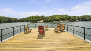 Eine Holzterrasse mit vier Stühlen und einem Tisch, mit Blick auf einen See mit bewaldetem Ufer.