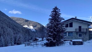 Paisaje nevado con una casa de fachada de piedra y un balcón.