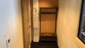 Un pasillo estrecho con techo de madera, una cama litera metálica, una puerta blanca y una ventana a la derecha.