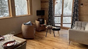 Interior acogedor de una cabaña con paredes de madera, un sofá, una mesa de comedor y grandes ventanales con vistas nevadas.