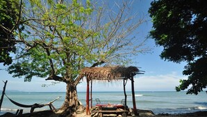 A beach scene with a thatched structure, a hammock, and a wooden table with chairs. - Welcome to my paradise! Cabina 2 (Puntarenas Province)