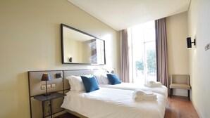 Ein Hotelzimmer mit einem großen Bett, einem Nachttisch mit Lampe, einem Sessel und einem Fenster mit Vorhängen.