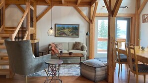 A cozy loft-style living room with a wooden staircase, a sofa, a coffee table, and a dining area with chairs. - Post and Beam Country home on 40 Acres of land in the Blaeberry Valley, Golden. (Golden)