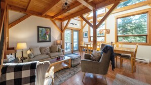 A spacious living room with wooden beams, a sofa, a coffee table, and a dining area with a table and chairs. - Post and Beam Country home on 40 Acres of land in the Blaeberry Valley, Golden. (Golden)