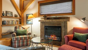 A cozy living room with a fireplace, wooden beams, a bookshelf, and comfortable seating. - Post and Beam Country home on 40 Acres of land in the Blaeberry Valley, Golden. (Golden)