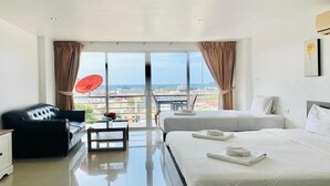 Une chambre d’hôtel avec un grand lit, un canapé, une petite table avec un vase, et une vue sur la ville grâce à de grandes fenêtres.