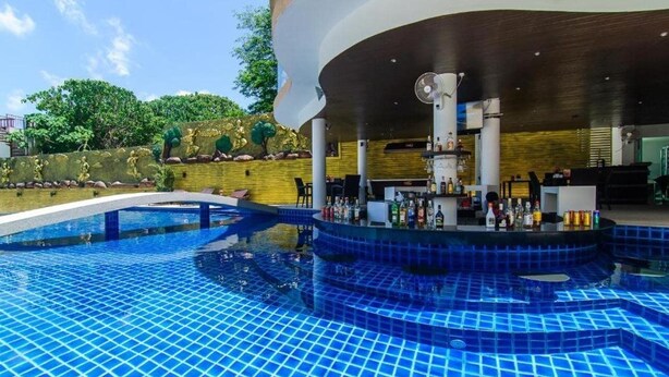 Une piscine dotée d’un espace bar, entourée d’une structure incurvée et agrémentée d’un mur décoratif recouvert de verdure.