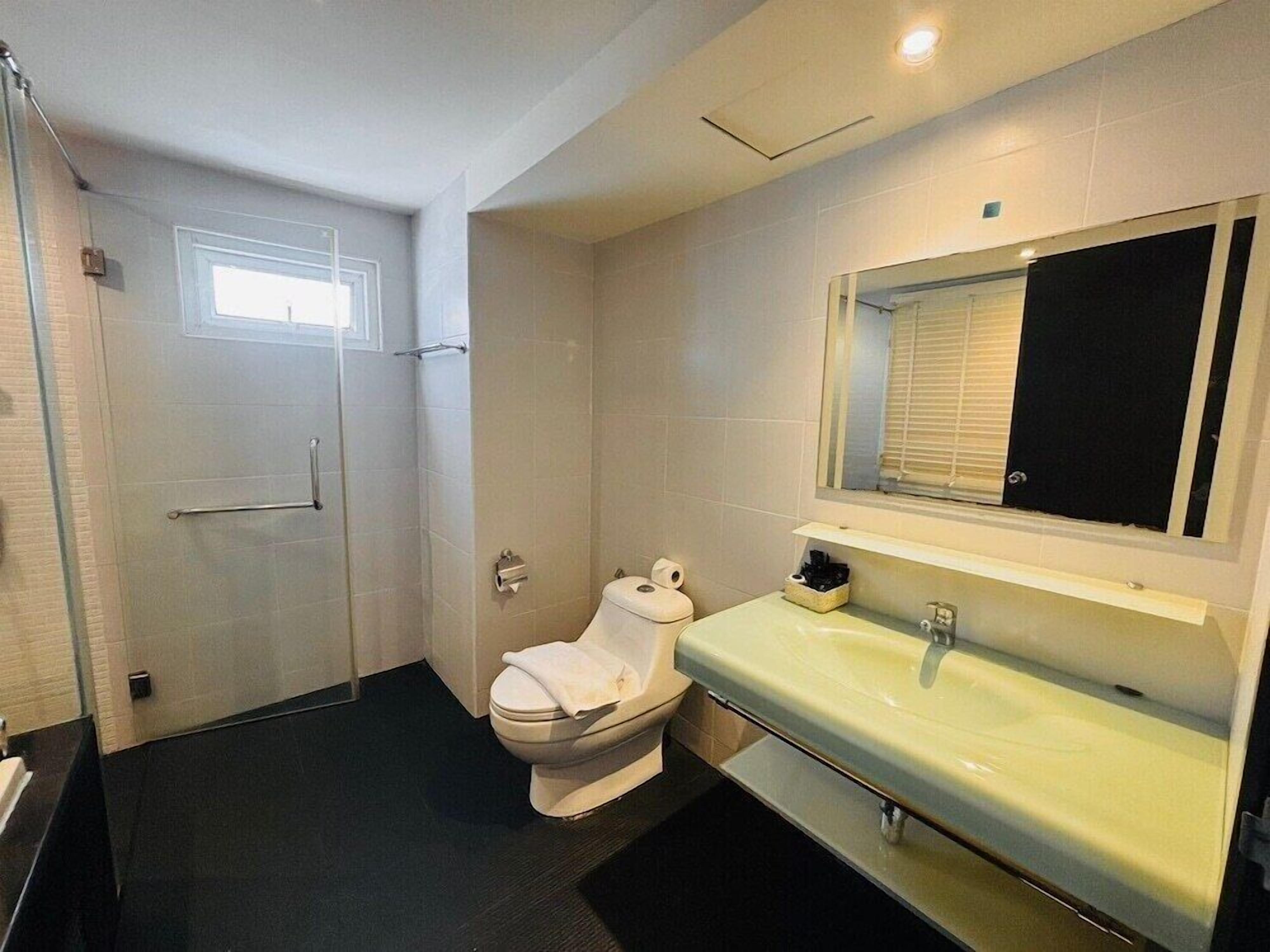 A bathroom with a toilet, sink, mirror, and shower.