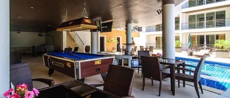 An outdoor pool area with a pool table, lounge chairs, and a covered seating area.