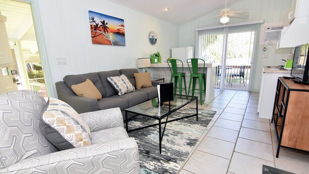 A living room with a sofa, coffee table, and patterned cushions. There is a dining area with green chairs and a table. A painting of a beach scene is on the wall. - Morningside (Sanibel)