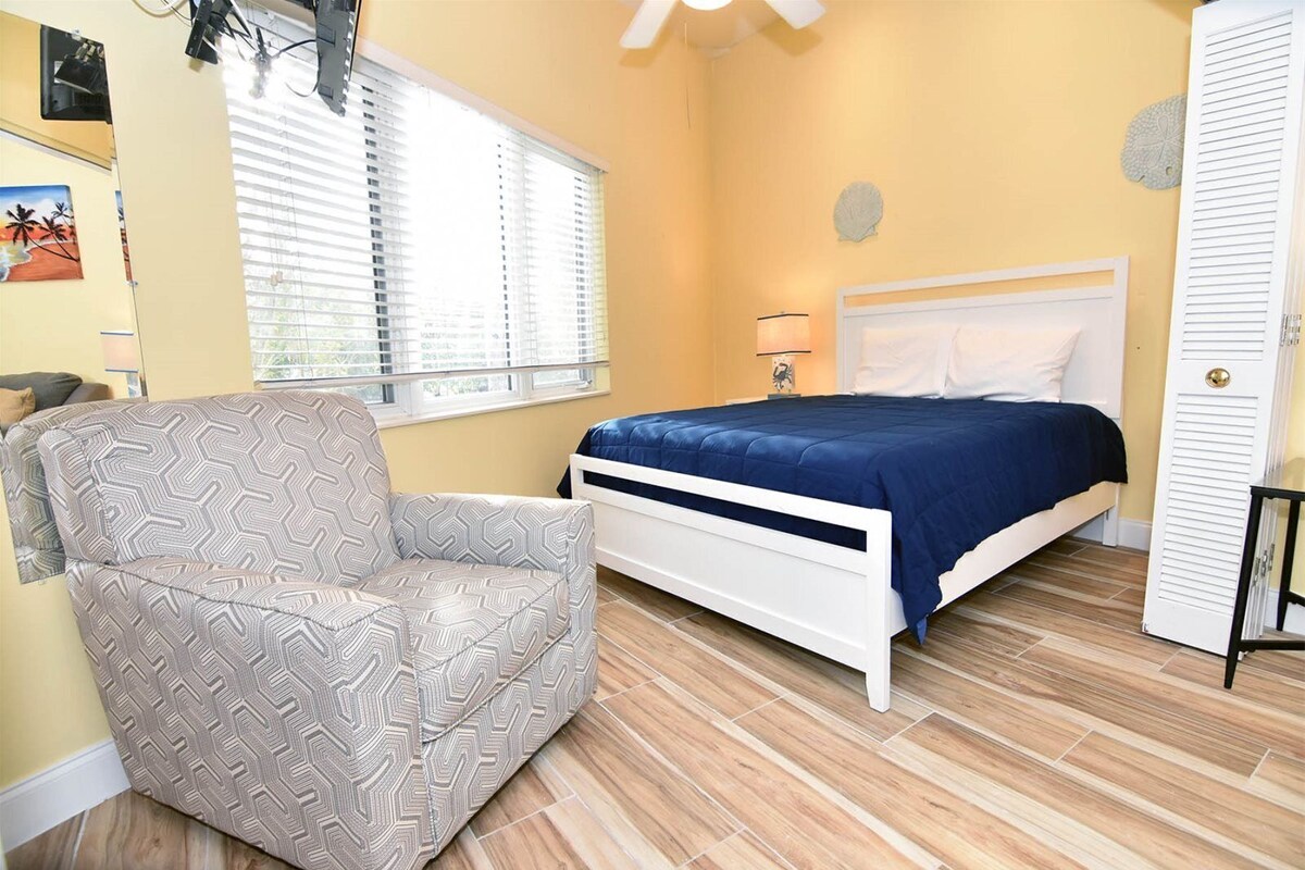 A bedroom with a bed, a chair, and a window with blinds.