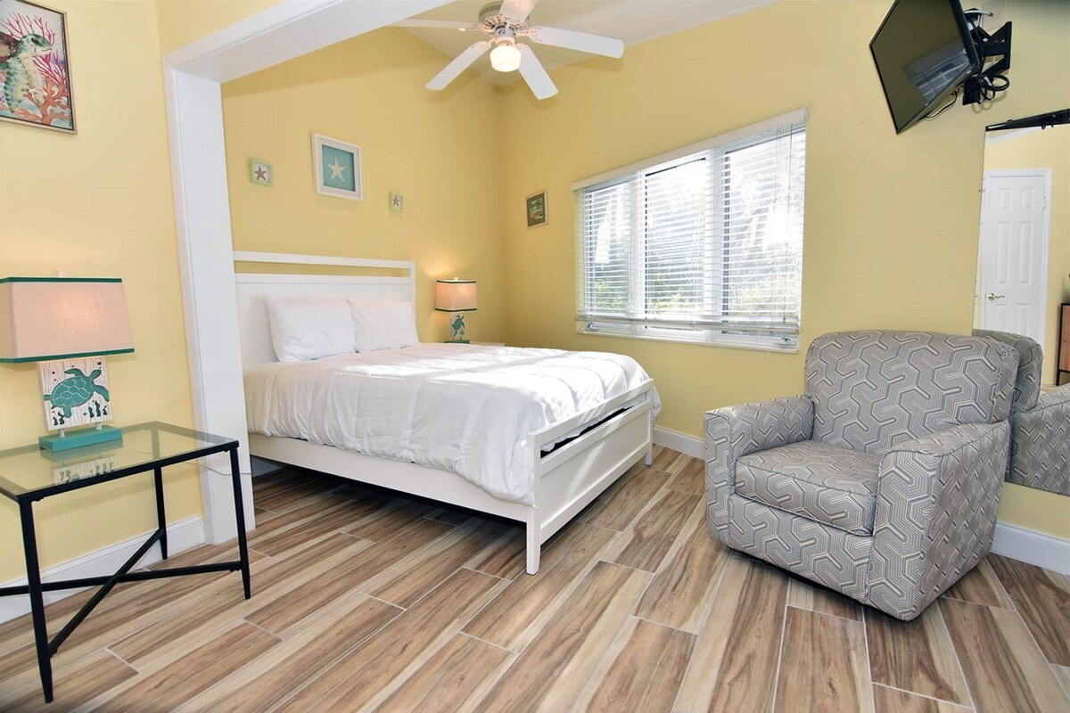 A bedroom with a bed, a chair, a nightstand, a lamp, and a ceiling fan.