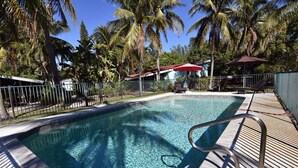 A clear swimming pool surrounded by palm trees and a fenced area with lounge chairs. - Morningside (Sanibel)