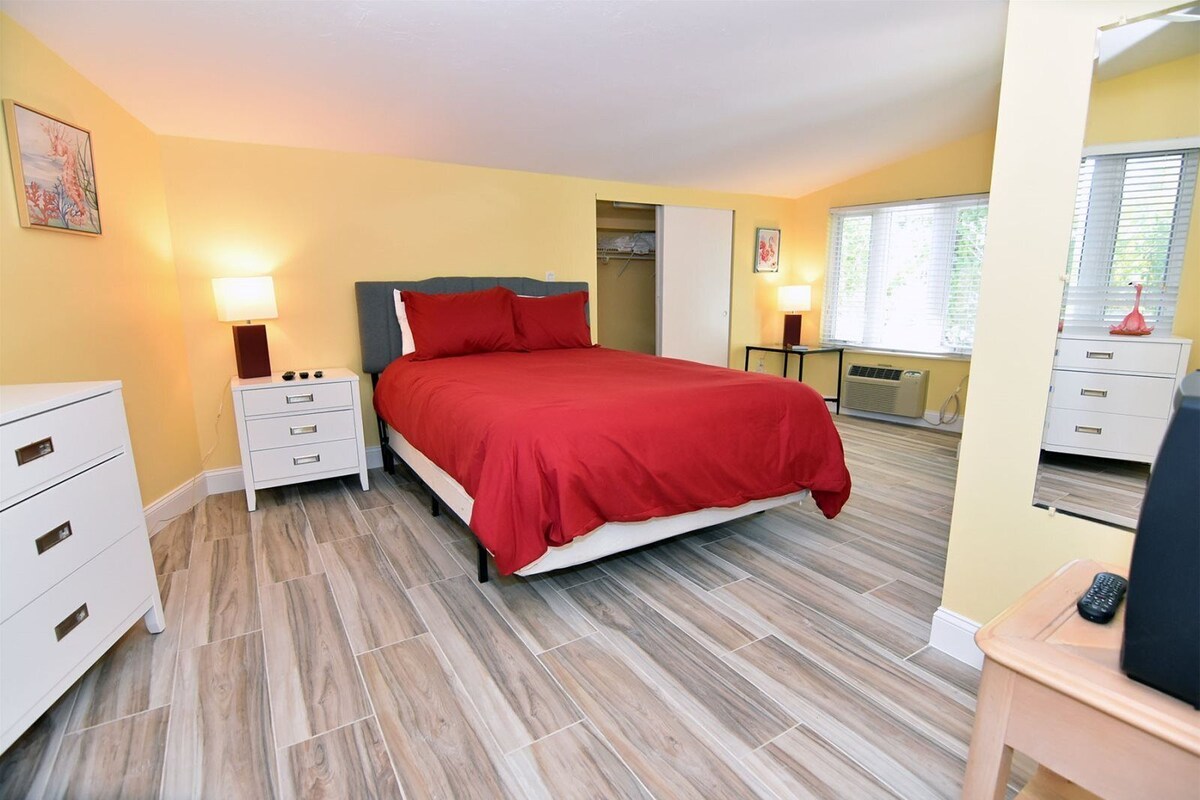 A bedroom with a bed, two bedside tables, a dresser, and a window with blinds.
