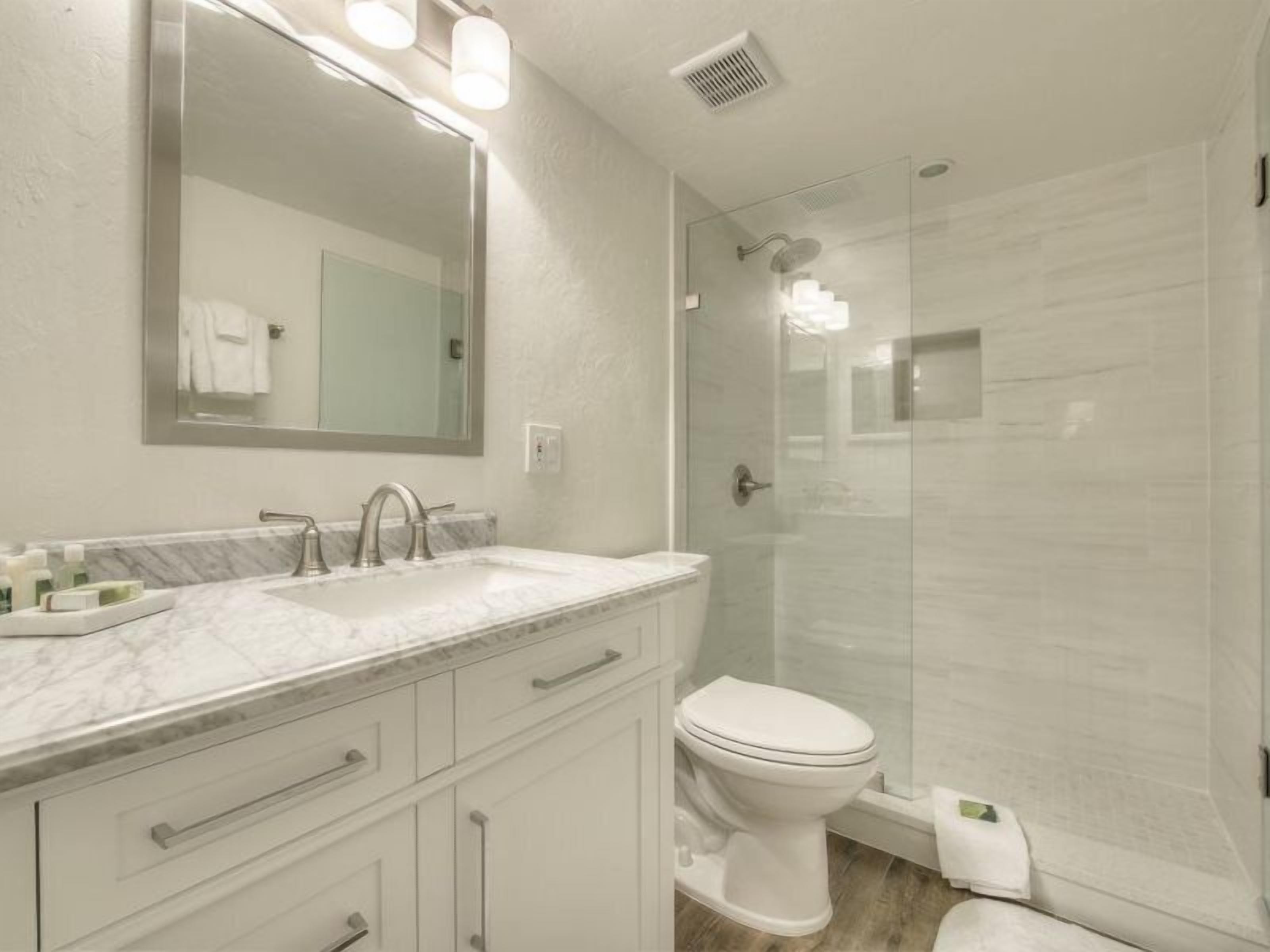 Un baño moderno con tocador de mármol, un espejo grande, inodoro y cabina de ducha con mampara de vidrio.